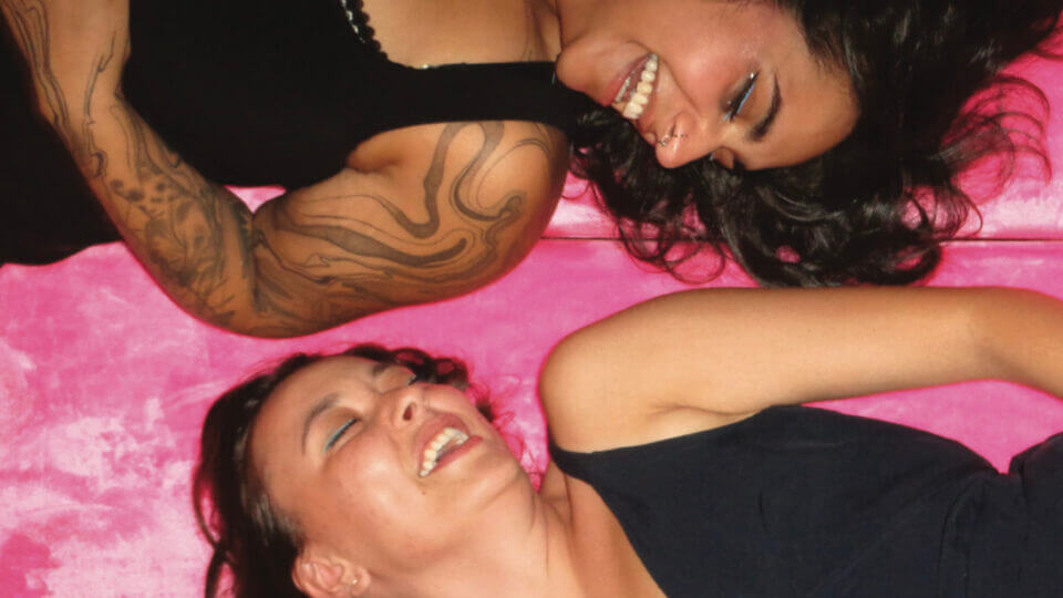 Kiona Callihoo and Sanaa Humayun lounge and laugh together on a fluffy pink blanket
