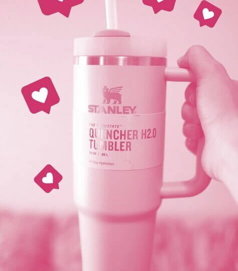 A Stanley quencher water bottle is tinted pink with several hearts around it to signify internet likes