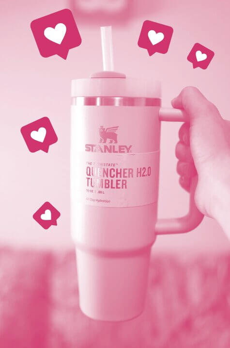 A Stanley quencher water bottle is tinted pink with several hearts around it to signify internet likes