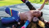 A person in rainbow clothing tackles another wrestler in the ring