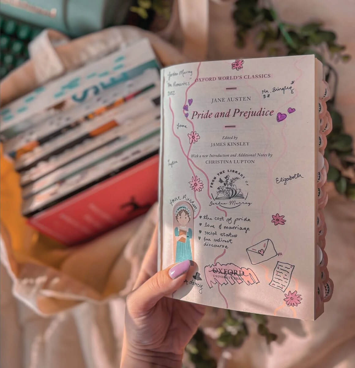 A photo of a hand holding up the inside cover page of Pride and Prejudice. It has been annotated with doodles. A bag full of books is out of focus in the background.