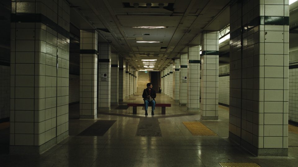 Photo of a person sitting on a bench on a dark subway platform.