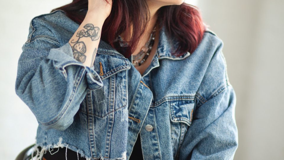 Photo of an Indigenous woman wearing a jean jacket sitting in a chair and looking off-camera.