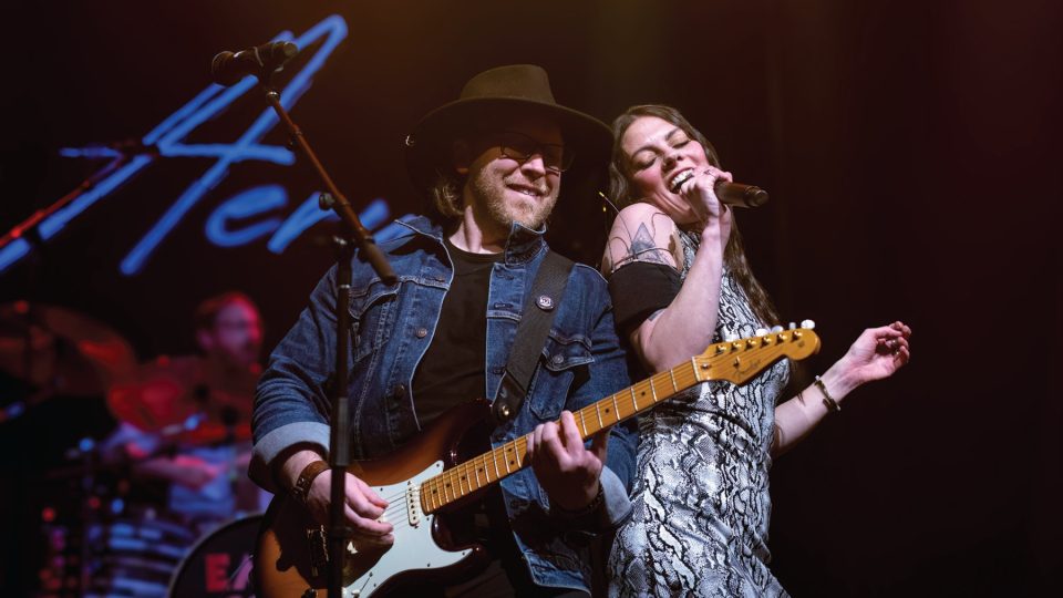 Photo of a man and a woman onstage performing with a guitar and microphone.