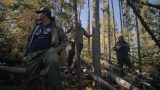 Photo of three Indigenous people walking through a forest.