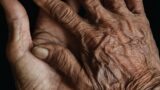 Close-up photo of wrinkled, brown hands against a black background.