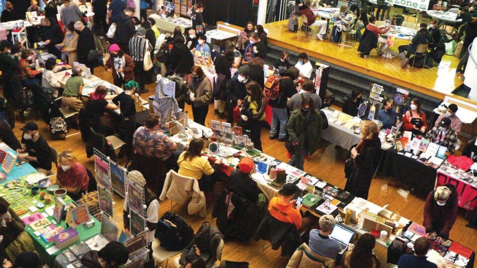 Overhead photo of a vendor hall filled with tables and people. A sign in the top right corner of the image reads 'Zine Making Zone.'